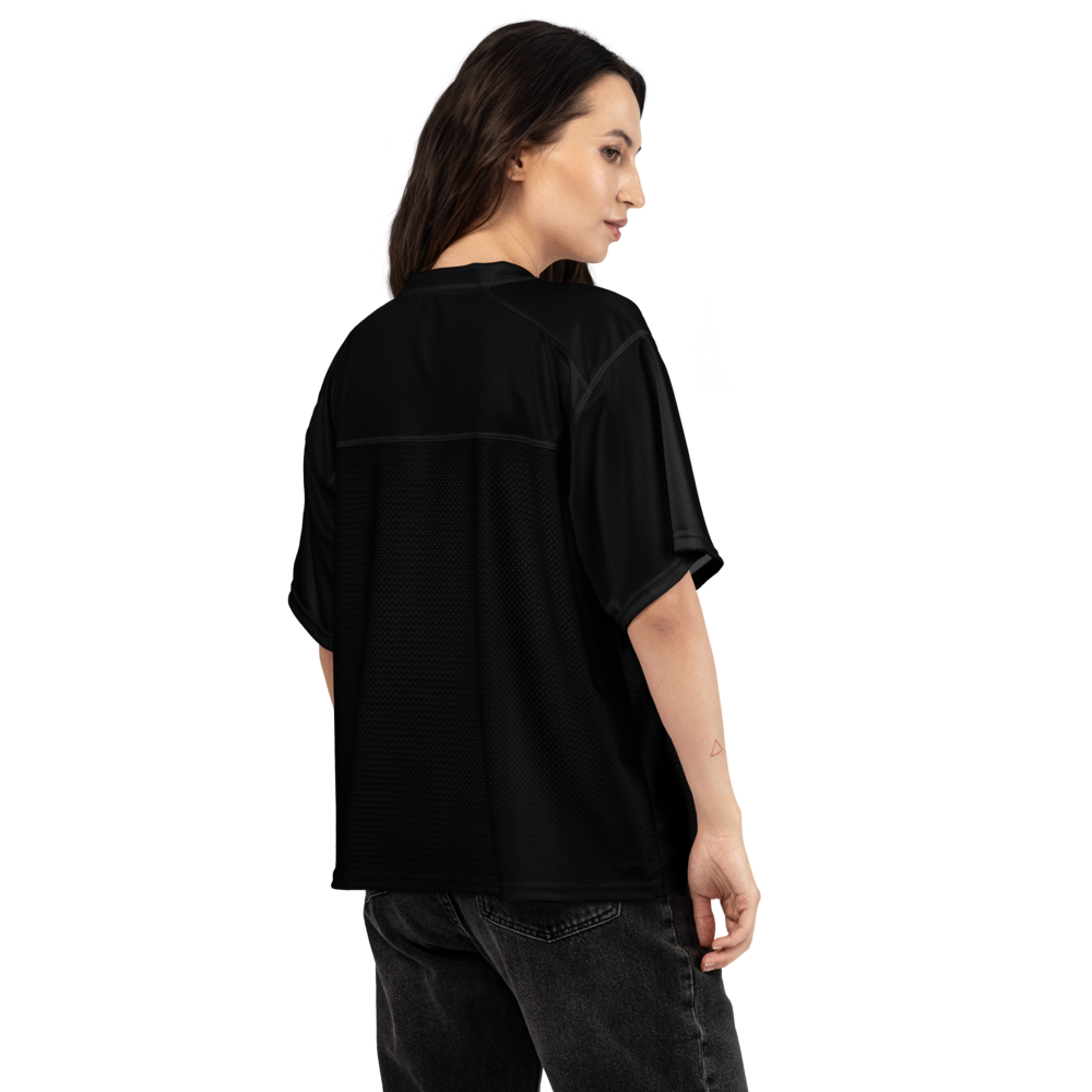 A woman shown from the back wearing a black short-sleeve athletic top with a subtle textured back panel, paired with dark gray jeans, against a plain white background.